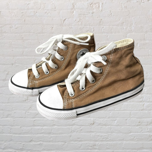 Tan Converse high-top sneakers with white laces and rubber soles, featured against a light brick background.