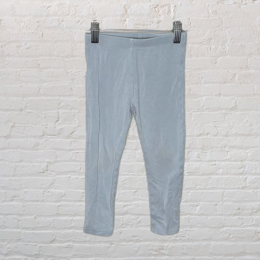 Light gray leggings displayed on a hanger against a white brick wall.