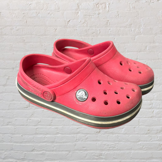 Pair of pink Crocs Classic Clogs with a white and black stripe on the sole, featuring ventilation holes and a strap.