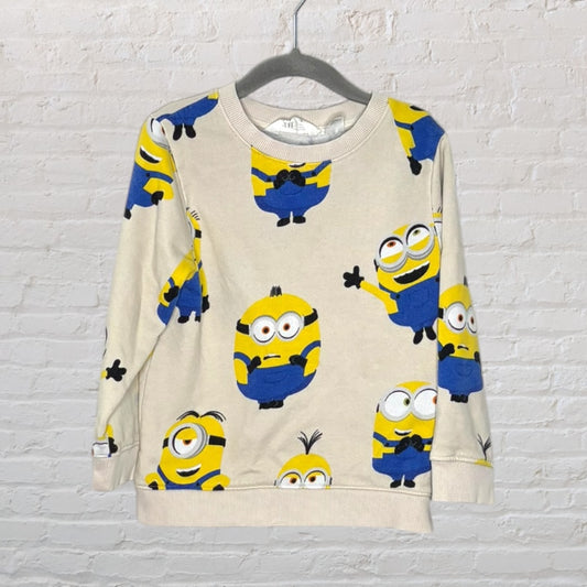 Beige sweatshirt with multiple Minion graphics in yellow and blue, long sleeves, hanging on a rack.