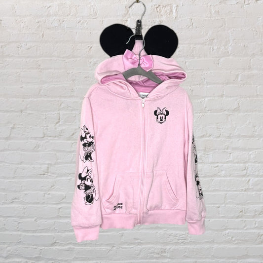 Pink Minnie Mouse zip-up hoodie featuring printed graphics on sleeves and hood with ear details, hung on a hanger.