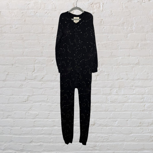 Black onesie sleepwear with constellation pattern, hanging against a white brick wall.