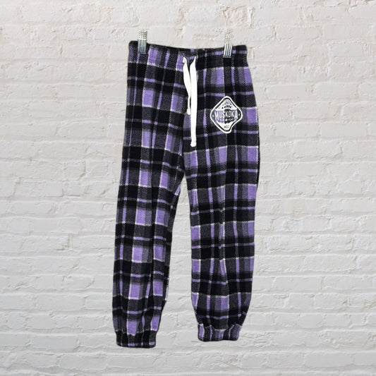 Purple and black plaid flannel pants with drawstring and Muskoka patch, hanging on a hanger.