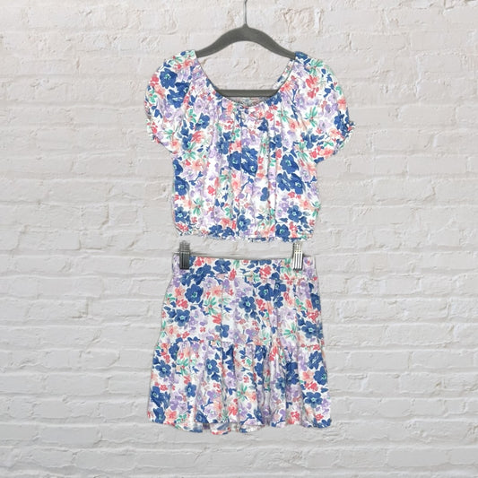 Women's floral crop top with matching skirt set in multicolor pattern, on hanger against a white brick wall.