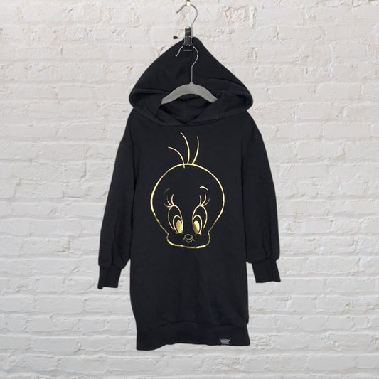 Black hoodie dress with a large gold graphic of Tweety Bird on the front, displayed on a hanger against a white brick wall.