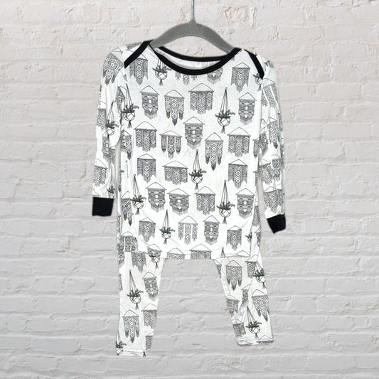 White pajama set with black geometric patterns and black cuffs, hanging against a brick wall.