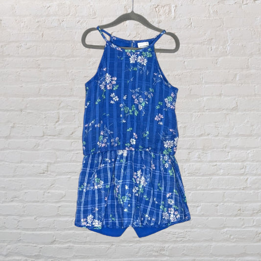 Blue romper with floral pattern, featuring a sleeveless design and cinched waist, hanging on a hanger.