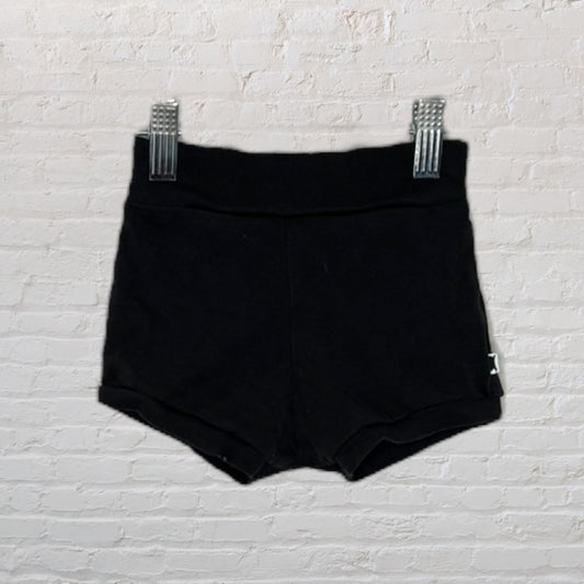 Black high-waisted shorts hanging on a white brick wall background.