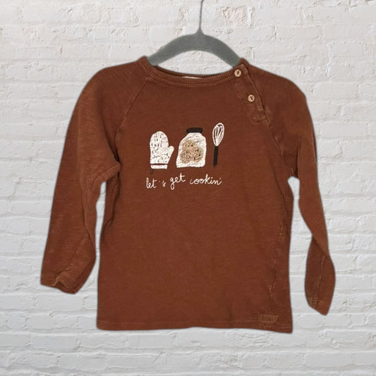 Brown long sleeve T-shirt with 'Let's Get Cookin'' graphic and kitchen items, featuring buttons on the shoulder.