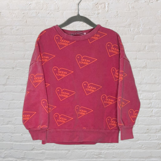 Red sweatshirt with orange 'Ocean Lovers' heart graphics, hanging on a black hanger.