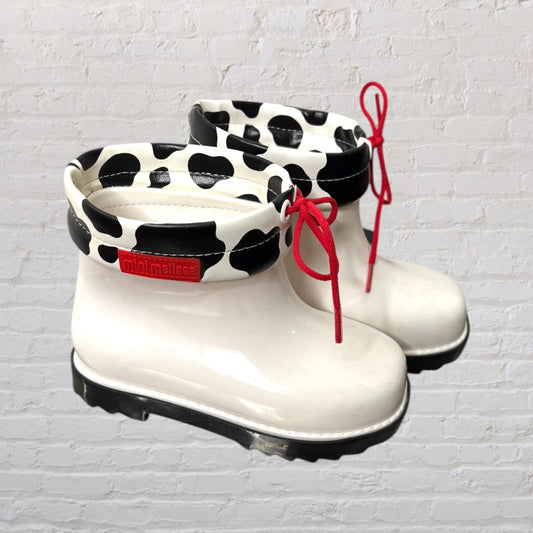 Mini Melissa cow print boots in white and black with red laces, featuring a playful design.