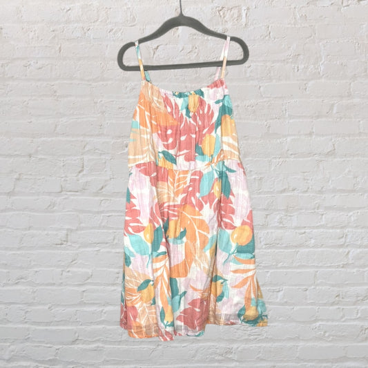 Multicoloured floral sundress with pastel hues and spaghetti straps, displayed on a hanger against a brick wall.