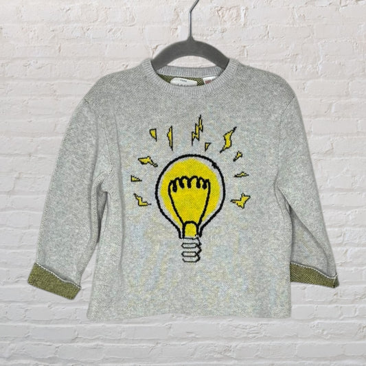 Grey sweater with a large graphic of a yellow light bulb and lightning bolts, designed by Zara, displayed on a hanger.