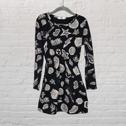 A black long sleeve dress with white rock-themed graphics including stars, guitars, and other motifs, displayed against a white brick wall.