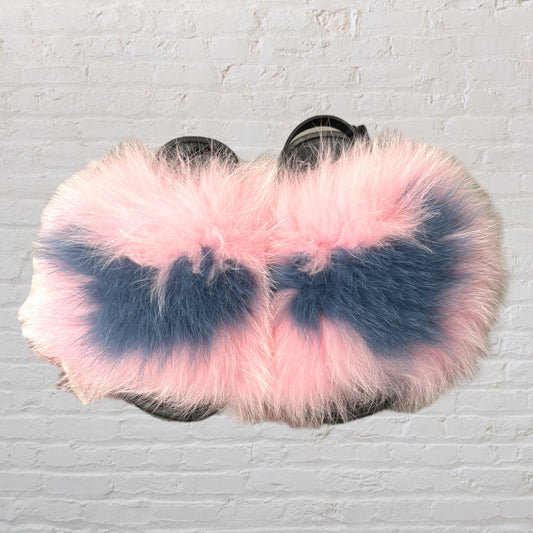 Pair of pink and blue faux fur slippers against a brick wall background.