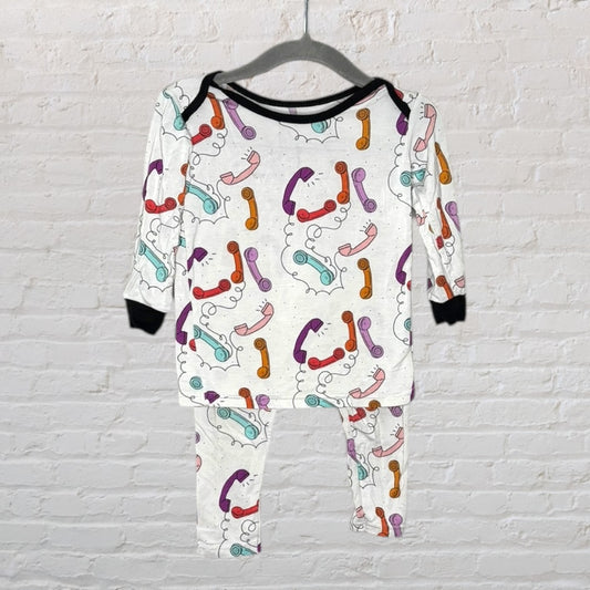 Unisex white pajama set featuring a colorful retro phone print, displayed on a hanger against a brick wall.