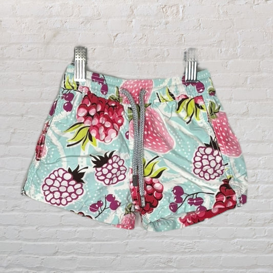 Mint green swim shorts with colorful fruit print and drawstring, displayed on hangers.