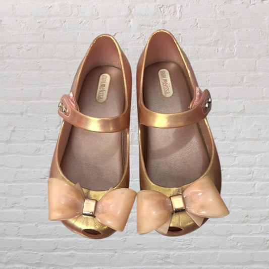 Pair of metallic peach Mini Melissa Mary Jane shoes with large bow detail and strap closure.