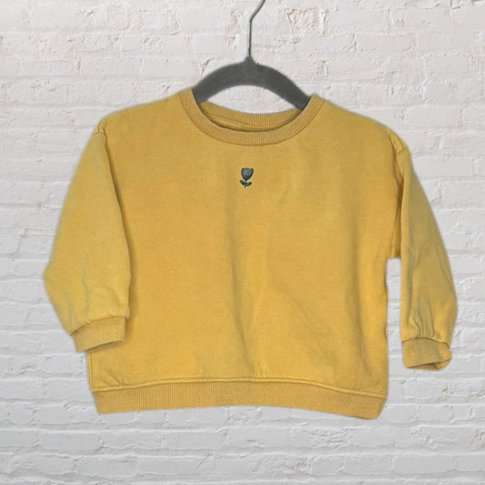 Yellow sweater with small embroidered flower detail in the center, displayed on a black hanger.