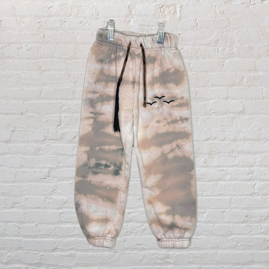 Unisex tie-dye sweatpants with black drawstring and bird motif, featuring beige and grey tones.